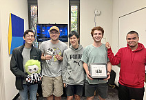 5 students at an escape room, holding a Beetlejuice doll and fake snake