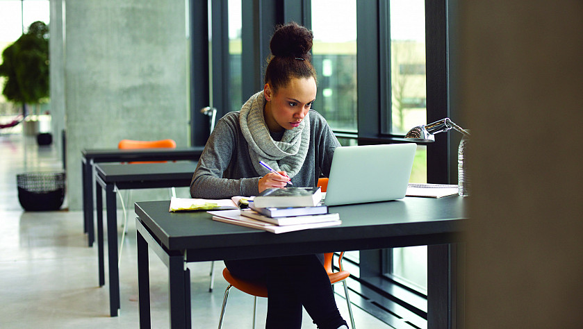 Student sitting at desk with books and laptop working in the library.