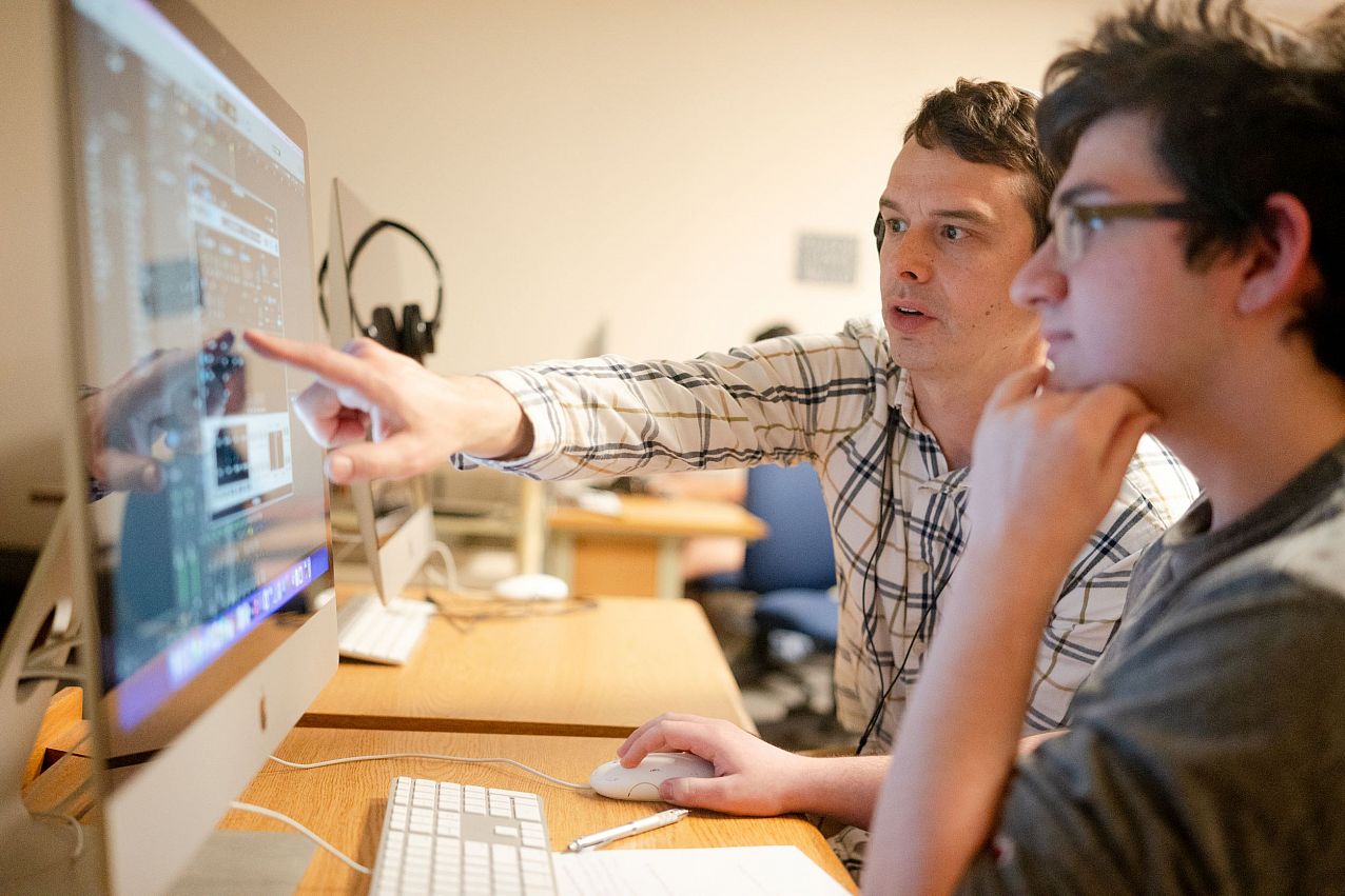 Graphic design student and faculty discussing application on desktop.