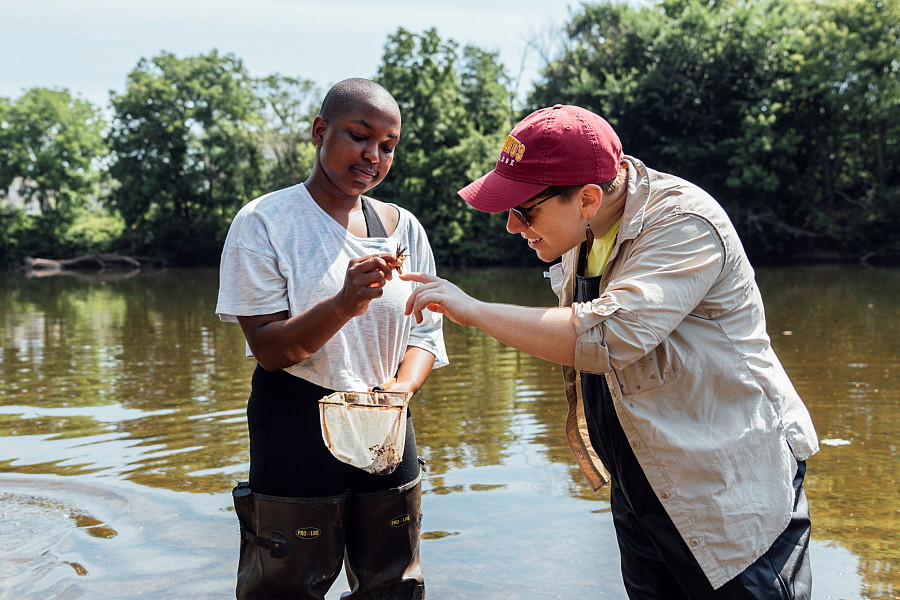Two students standing in a lake looking at a fish they caught.