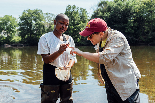 Two students standing in a lake looking at a fish they caught.