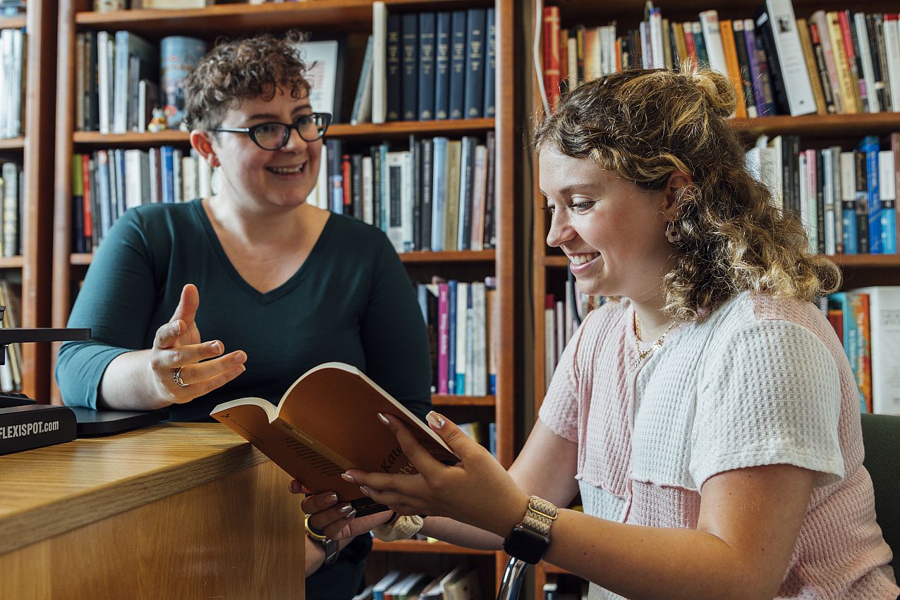 Dr. McShane sitting in public library with student discussing a topic from open book.