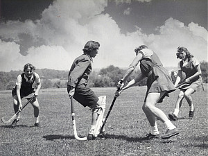 An old black and white photograph of students playing felid hockey together outside.