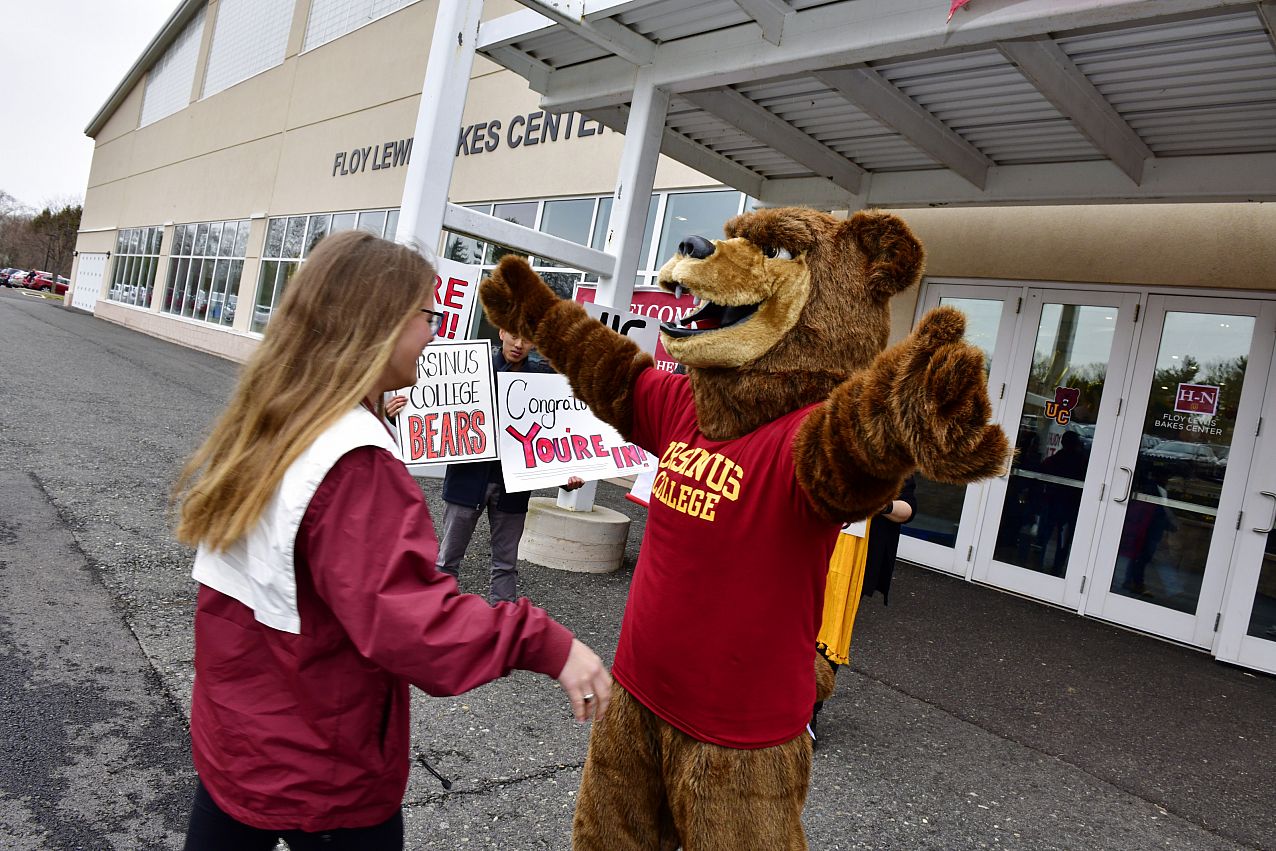 Ursinus College bear mascot about to give hug to student outside.