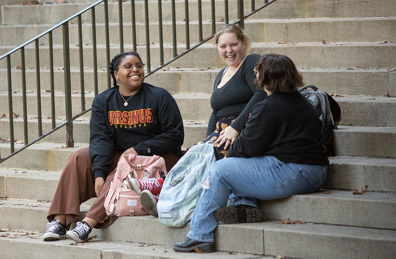 Three students sitting on outside steps talking.
