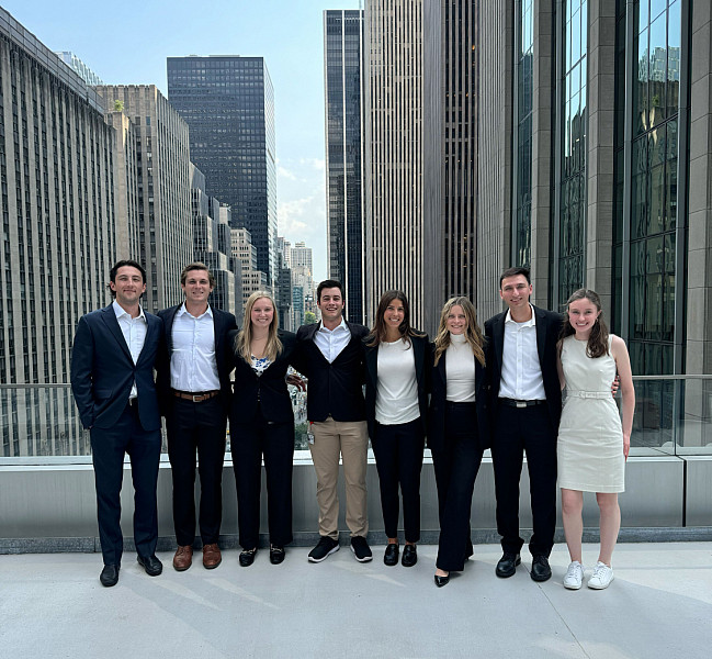 Group photo of students dressed in business professional standing on a roof top in a city.