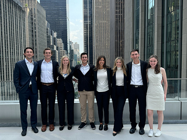 Group photo of students dressed in business professional standing on a roof top in a city.