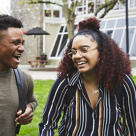 Two students laughing while walking through campus.