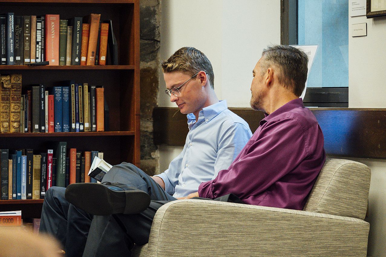 Two college students sitting in library reading a book.